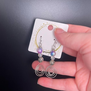 May include: A pair of silver earrings with iridescent purple and white beads, a silver bead, and a spiral design.