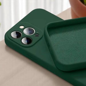 May include: A dark green phone case with a matte finish. The case is shown with the camera lens cutouts visible. The interior of the case is a lighter shade of green. The case is designed to protect the phone.