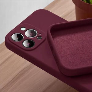 May include: A burgundy-colored phone case with a soft, matte finish. The case is shown with the phone, highlighting the camera lenses. The interior of the case is also burgundy. The phone case is designed to protect the phone.