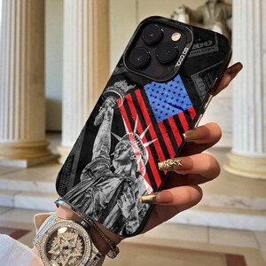May include: Black phone case with a design of the Statue of Liberty and the American flag. The case has a black background with a design of dollar bills. The text "SO COOL" is printed on the side of the case.