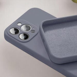 May include: A close-up of a periwinkle-colored phone case with a soft, matte finish. The case is open, revealing the interior lining. The phone's camera lenses are visible.