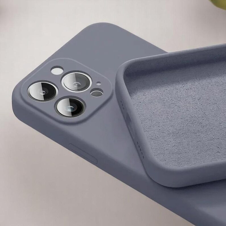 May include: A close-up of a periwinkle-colored phone case with a soft, matte finish. The case is open, revealing the interior lining. The phone's camera lenses are visible.