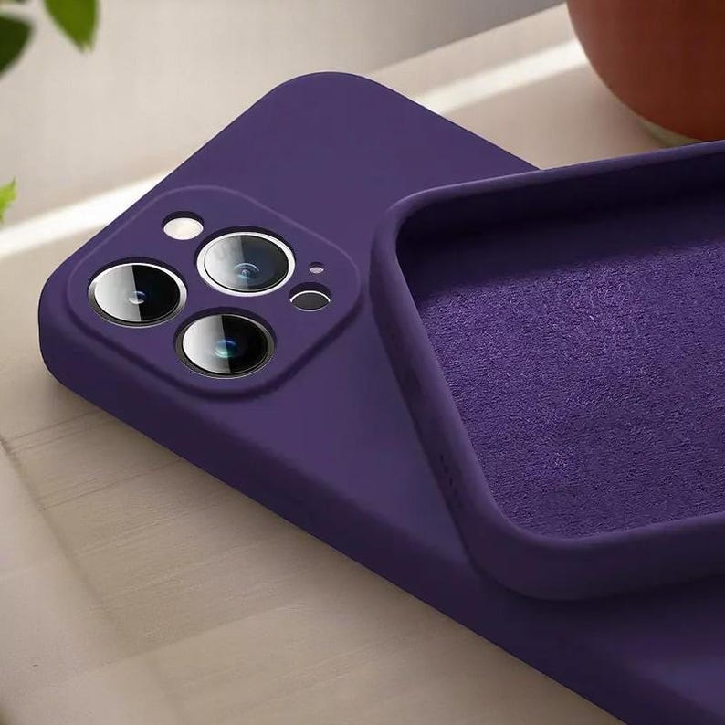 May include: A close-up of a purple phone case with a camera cutout. The case is made of a smooth material and has a soft interior. The camera lenses are visible.