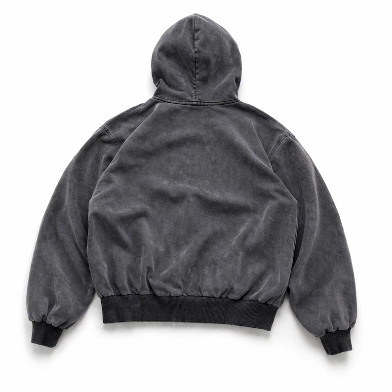 Puede incluir: Una sudadera con capucha gris carb&oacute;n con una apariencia descolorida y vintage. La vista trasera muestra una sudadera con capucha con cord&oacute;n, mangas largas y dobladillo y pu&ntilde;os acanalados. La tela tiene una textura suave y desgastada.