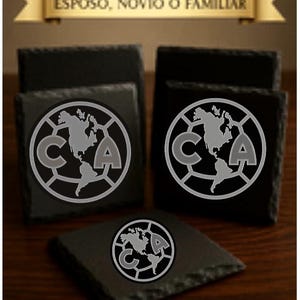 May include: Four black slate coasters with a silver graphic of a soccer ball with a world map inside and the letters "CA" on either side. The text "PERFECTO PARA PAPA, ESPOSO, NOVIO O FAMILIAR" is on a gold ribbon above the coasters.