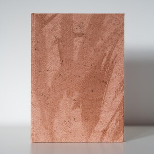 Puede incluir: Un objeto rectangular de color marrón rojizo con una superficie texturizada. El objeto tiene un aspecto rugoso e irregular, con sutiles variaciones de color y tono. La impresión general es de un material natural y terroso.