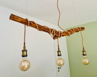 May include: A rustic, wooden pendant light fixture. A natural, brown branch is wrapped with rope and suspends three Edison-style light bulbs. The light bulbs have a warm, amber glow, and the fixture hangs from the ceiling.