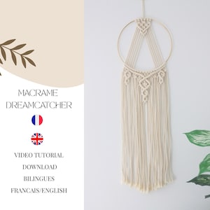 May include: A cream-colored macrame dreamcatcher with a gold-colored metal ring. The dreamcatcher features intricate knotting patterns and long, flowing fringe. The image also includes text that reads "MACRAME DREAMCATCHER" and "VIDEO TUTORIAL DOWNLOAD BILINGUES FRANCAIS/ENGLISH".