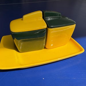 May include: A yellow ceramic serving tray with two small ceramic containers. The containers have green lids and yellow bases.