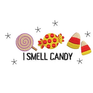 May include: An embroidered design featuring a purple and tan lollipop, a yellow candy with red dots, and two candy corn pieces. The phrase "I SMELL CANDY" is written below the candies, with black star accents.