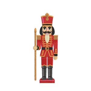 Puede incluir: Una figura de cascanueces roja y dorada con bigote negro, botas negras y un bastón dorado. El cascanueces lleva un sombrero y una chaqueta rojos con adornos dorados y un cinturón negro. La figura está sobre una base roja.