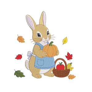 May include: An embroidered design of a tan rabbit wearing a blue apron, holding an orange pumpkin. Beside the rabbit is a brown woven basket containing a red apple and yellow pears, surrounded by scattered autumn leaves in red, yellow, and green.