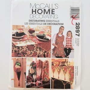 May include: A McCall's Home Decorating pattern envelope. The cover features images of table settings, aprons, and decorative items. The text includes "Decorating Essentials" and "Les Essentials de Decoration". The pattern number is 2897.