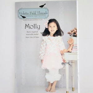 May include: A magazine cover featuring a young girl wearing a pink and white dress. The cover reads "Violette Field Threads" and "Molly" with text indicating a retro-inspired reversible jacket pattern for sizes 12 months to 10 years.