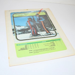 May include: Vintage children's vest sewing pattern. The pattern features a color image of children wearing the vest while snowshoeing. The pattern includes body measurements and supply details. The background is a white surface.