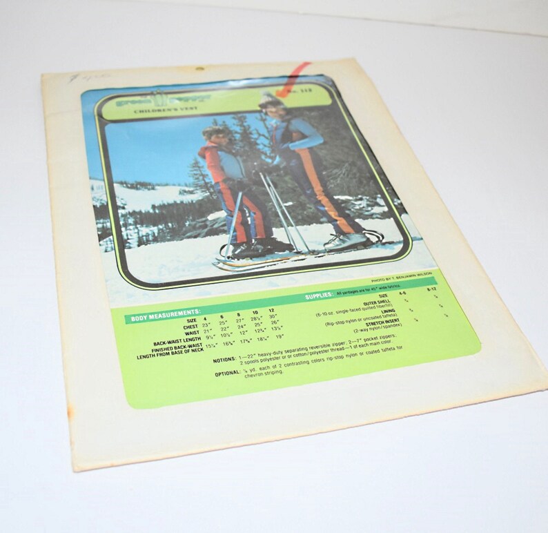 May include: Vintage children's vest sewing pattern. The pattern features a color image of children wearing the vest while snowshoeing. The pattern includes body measurements and supply details. The background is a white surface.