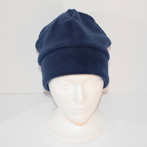 May include: A navy blue fleece beanie hat. The hat is displayed on a white mannequin head. The hat has a folded brim and a rounded top. The fleece material appears soft and warm. The hat is a solid color and suitable for cold weather.