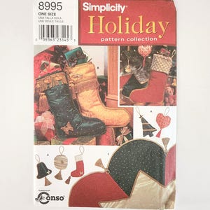 Könnte beinhalten: Simplicity Holiday Schnittmusterkollektion mit verschiedenen Designs für Weihnachtsstrümpfe und -ornamente. Das Cover zeigt Bilder von fertigen Strümpfen in Grün, Gold und Rot sowie Ornamentmustern. Der Text "ONE SIZE" ist sichtbar.