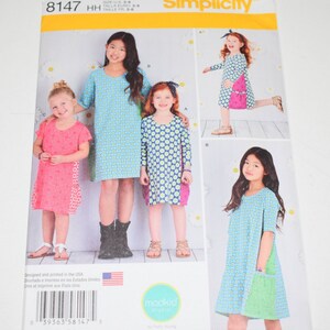 May include: Simplicity sewing pattern 8147 for girls' dresses. The pattern features multiple dress designs with various sleeve lengths and pocket styles. The cover shows children wearing the dresses, with a blue and green floral pattern. The size range is U.S. 3-6.