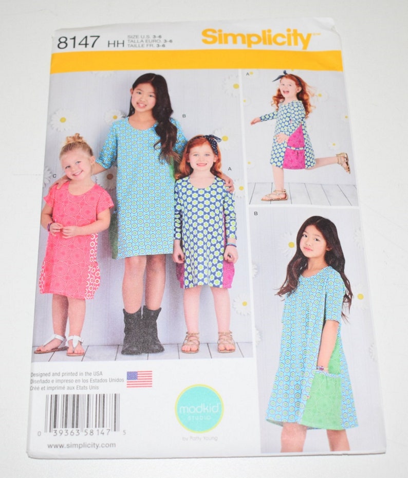 May include: Simplicity sewing pattern 8147 for girls' dresses. The pattern features multiple dress designs with various sleeve lengths and pocket styles. The cover shows children wearing the dresses, with a blue and green floral pattern. The size range is U.S. 3-6.
