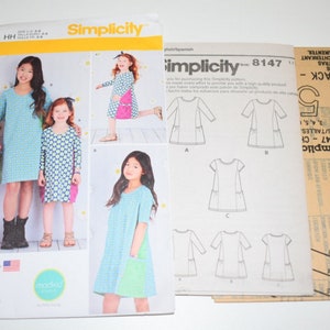 May include: Simplicity sewing pattern 8147 for girls' dresses. The pattern envelope features images of the finished dresses in various colors and patterns. Includes pattern pieces and instructions for different dress styles.