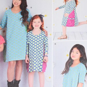 May include: Image of children's dresses. The dresses feature a blue and green floral pattern. One dress has a pink pocket. The dresses have different sleeve lengths. The background has a daisy pattern.