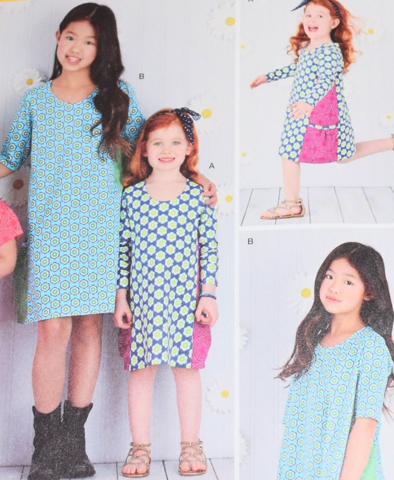May include: Image of children's dresses. The dresses feature a blue and green floral pattern. One dress has a pink pocket. The dresses have different sleeve lengths. The background has a daisy pattern.