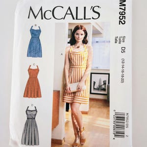 May include: McCall's sewing pattern M7952 featuring a woman in a striped dress. The pattern includes illustrations of various dress styles, including a denim-look dress, an orange dress, and a black and white patterned dress. The size is D5 (12-14-16-18-20).
