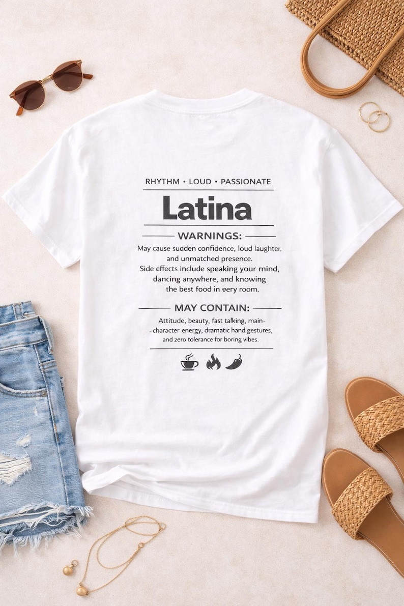 May include: White t-shirt with the word "Latina" printed in black, and a list of "warnings" and "may contain" attributes. The shirt is displayed with sunglasses, sandals, and denim shorts.