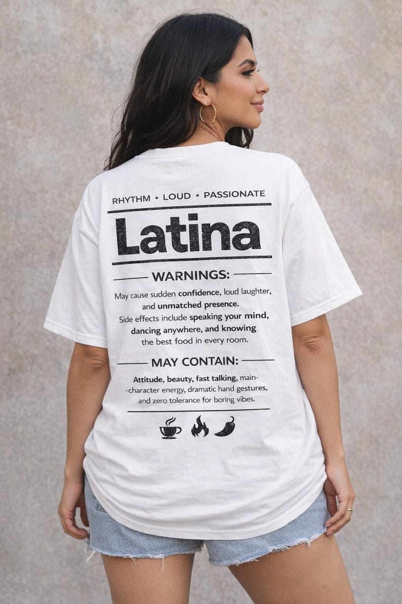 May include: White t-shirt with the word "Latina" in bold black letters. The shirt includes text about confidence, laughter, and attitude. The shirt has a crew neck and short sleeves.