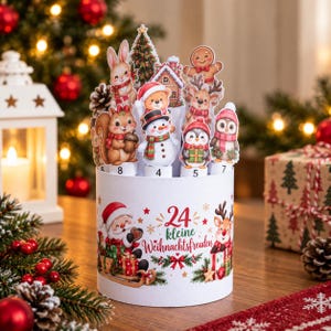 May include: A cylindrical white cardboard advent calendar featuring the text 24 kleine Weihnachtsfreuden. The top displays die-cut illustrations of a rabbit, squirrel, snowman, gingerbread person, reindeer, penguin, and owl among trees.