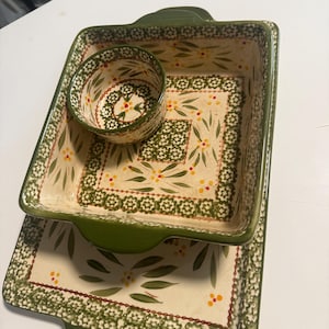 May include: A ceramic kitchen set consisting of a rectangular tray with handles, a square baking dish with handles, and a small round bowl. Each piece features a cream-colored base with a green floral pattern, green borders, and small yellow accents.