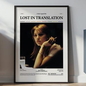 May include: Framed movie poster for "Lost in Translation" featuring a woman with blonde hair holding a cigarette. The poster has a black frame and is displayed on a white wall. The poster includes the movie title and credits.