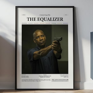 Puede incluir: Un póster enmarcado de la película "The Equalizer" con Denzel Washington sosteniendo un arma. El póster tiene un marco negro y se muestra contra una pared blanca. El póster incluye el título de la película y los créditos.
