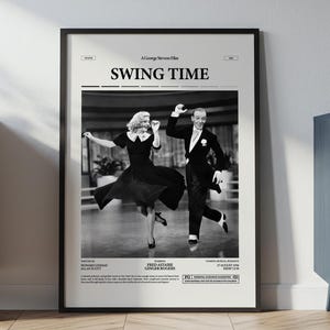 Puede incluir: Póster enmarcado en blanco y negro de la película "Swing Time". El póster presenta a una pareja bailando con ropa formal. El póster se exhibe en una pared blanca, junto a un mueble de madera y un mueble azul.