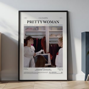 May include: A framed movie poster for "Pretty Woman" with a black frame. The poster features a scene from the film with two women in a clothing store. The poster is displayed on a wall next to a wooden cabinet.