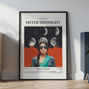 Può includere: Un poster incorniciato con il titolo "SISTER MIDNIGHT" presenta una donna con occhiali da sole, sullo sfondo di fasi lunari e un paesaggio urbano. Il poster ha una cornice nera ed è esposto su una parete vicino a un mobile in legno.