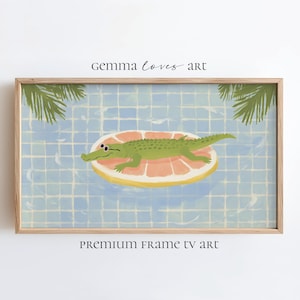 May include: A framed print featuring a whimsical illustration of a green alligator floating on a grapefruit-shaped pool float in a blue tiled pool. The artwork includes the text "gemma loves art" and "PREMIUM FRAME TV art".