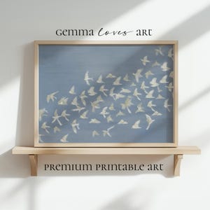Puede incluir: Una impresión enmarcada que presenta una bandada de pájaros color crema sobre un fondo azul apagado. La obra de arte se exhibe en una estantería de madera clara, con el texto "GEMMA LOVES ART" y "PREMIUM PRINTABLE ART" visible.