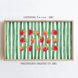 Könnte beinhalten: Ein gerahmtes Aquarellbild von roten Erdbeeren auf einem grün-weiß gestreiften Hintergrund. Der Text "gemma loves art" befindet sich oben im Bild und "premium frame tv art" unten.