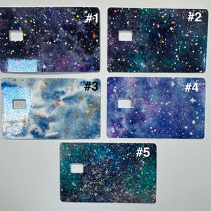 May include: Five rectangular card covers with a cutout, each showcasing a unique galaxy design. The designs feature swirling blues, purples, and greens with sparkling stars and glitter effects. Each card is labelled with a number.