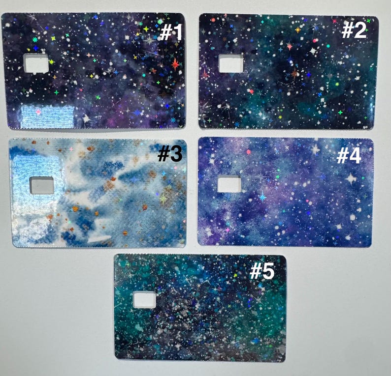 May include: Five rectangular card covers with a cutout, each showcasing a unique galaxy design. The designs feature swirling blues, purples, and greens with sparkling stars and glitter effects. Each card is labelled with a number.