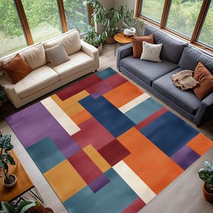May include: A colorful geometric area rug with a modern design. The rug features a pattern of overlapping rectangles in shades of purple, blue, orange, red, and cream. The rug is placed in a living room setting with two sofas and large windows.