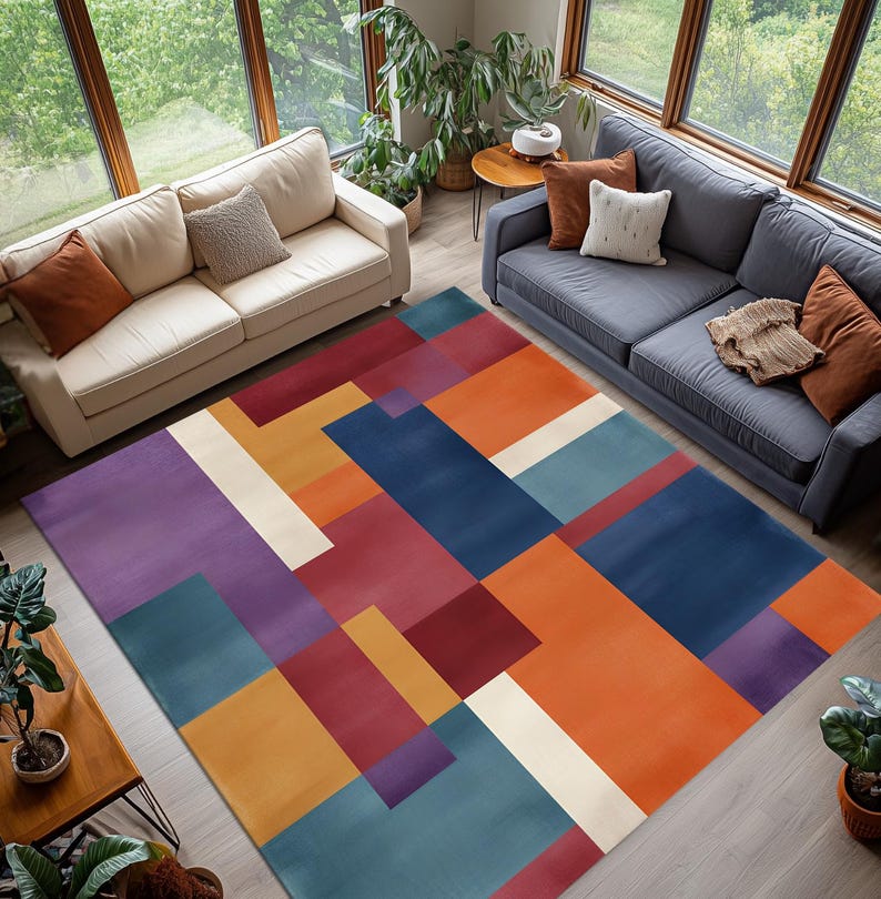 May include: A colorful geometric area rug with a modern design. The rug features a pattern of overlapping rectangles in shades of purple, blue, orange, red, and cream. The rug is placed in a living room setting with two sofas and large windows.