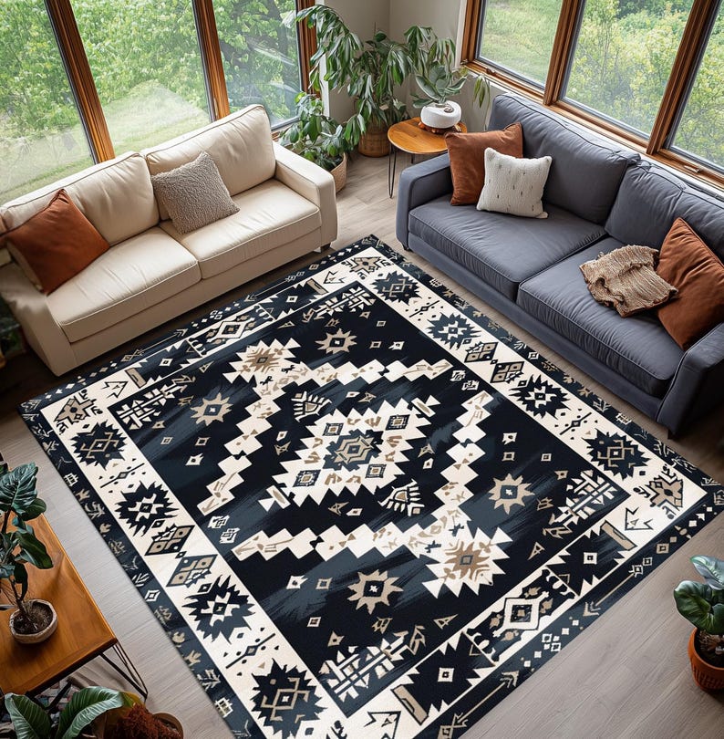 May include: A large, rectangular area rug with a geometric pattern in shades of navy, cream, and tan. The rug features a central design with repeating shapes and a border with similar motifs. The rug is placed in a living room setting with sofas and plants.