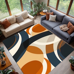 May include: A large, rectangular rug with an abstract design. The rug features a pattern of overlapping shapes in shades of navy blue, cream, orange, and brown. The rug is placed in a living room with two sofas and large windows.