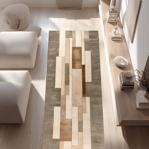 Puede incluir: Vista aérea de una alfombra rectangular con diseño geométrico. La alfombra presenta un patrón de rectángulos verticales en tonos beige, marrón y gris. Está colocada sobre un suelo de madera clara, con asientos y cojines blancos al fondo. Dimensiones: aprox. 200cm x 300cm.