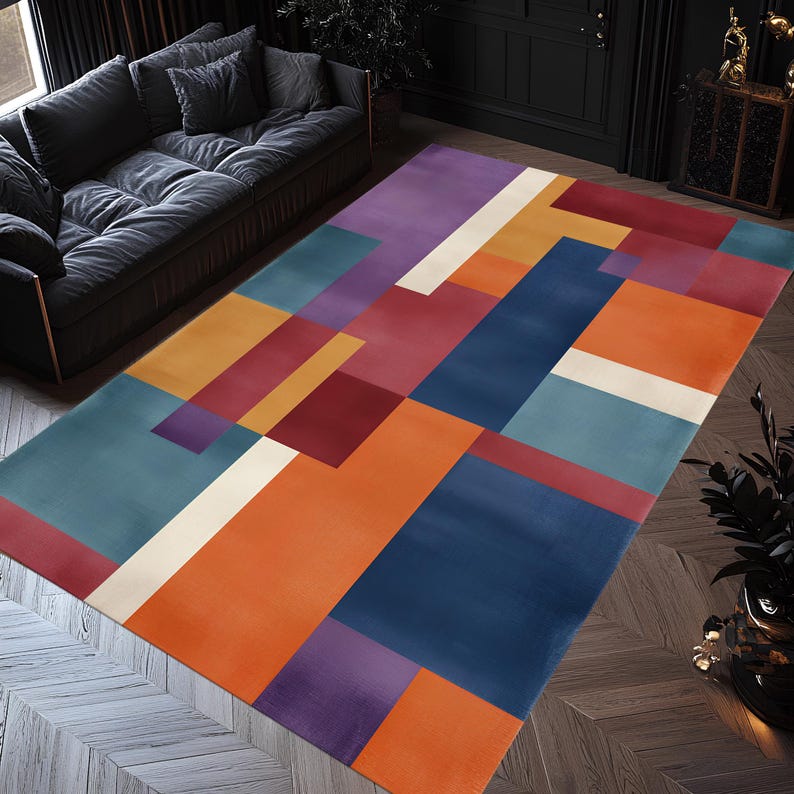 May include: A rectangular area rug with a geometric design. The rug features blocks of color in shades of orange, blue, purple, red, and white. The rug is placed on a wooden floor, and a dark gray sofa is visible in the background.