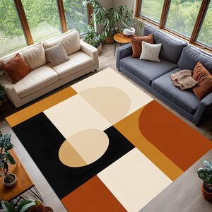 May include: A geometric area rug with a modern design. The rug features a pattern of black, cream, tan, and rust-colored shapes. The rug is rectangular and covers a large area of the room. The rug is placed in a living room with two sofas and large windows.