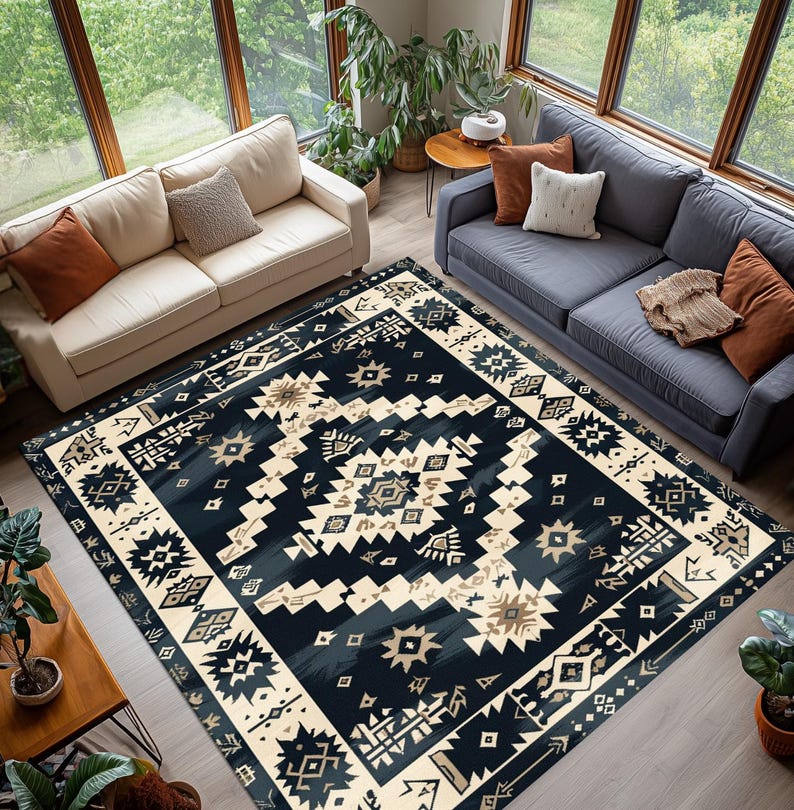 May include: A large area rug with a geometric pattern in navy blue, cream, and tan. The rug features a central design with repeating shapes and a border with similar motifs. The rug is placed in a living room with two sofas and large windows.